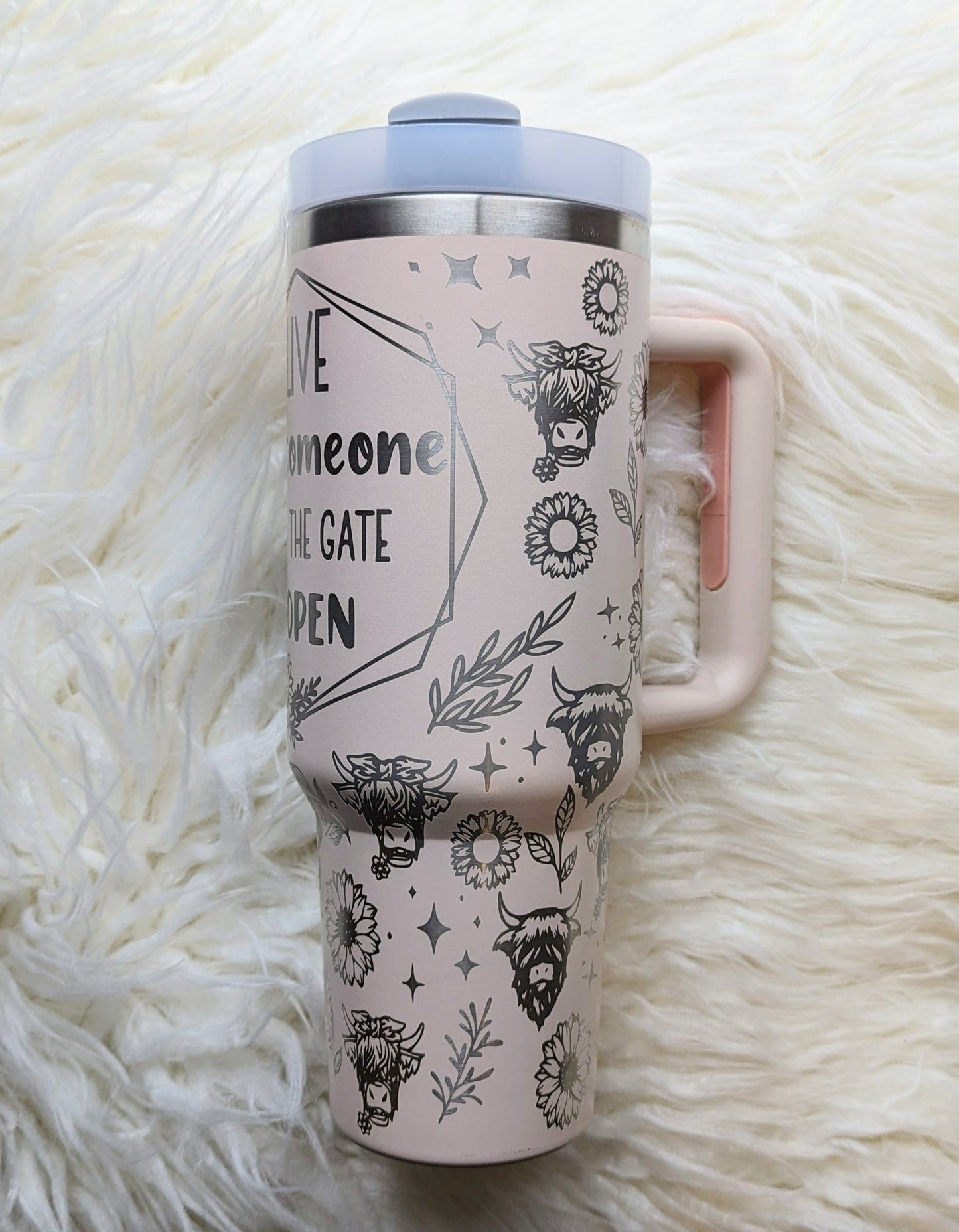 Photo of a soft pink colored 40 oz insulated tumbler with handle permanently engraved with a highland cow pattern and the text Live Like Someone Left the Gate Open