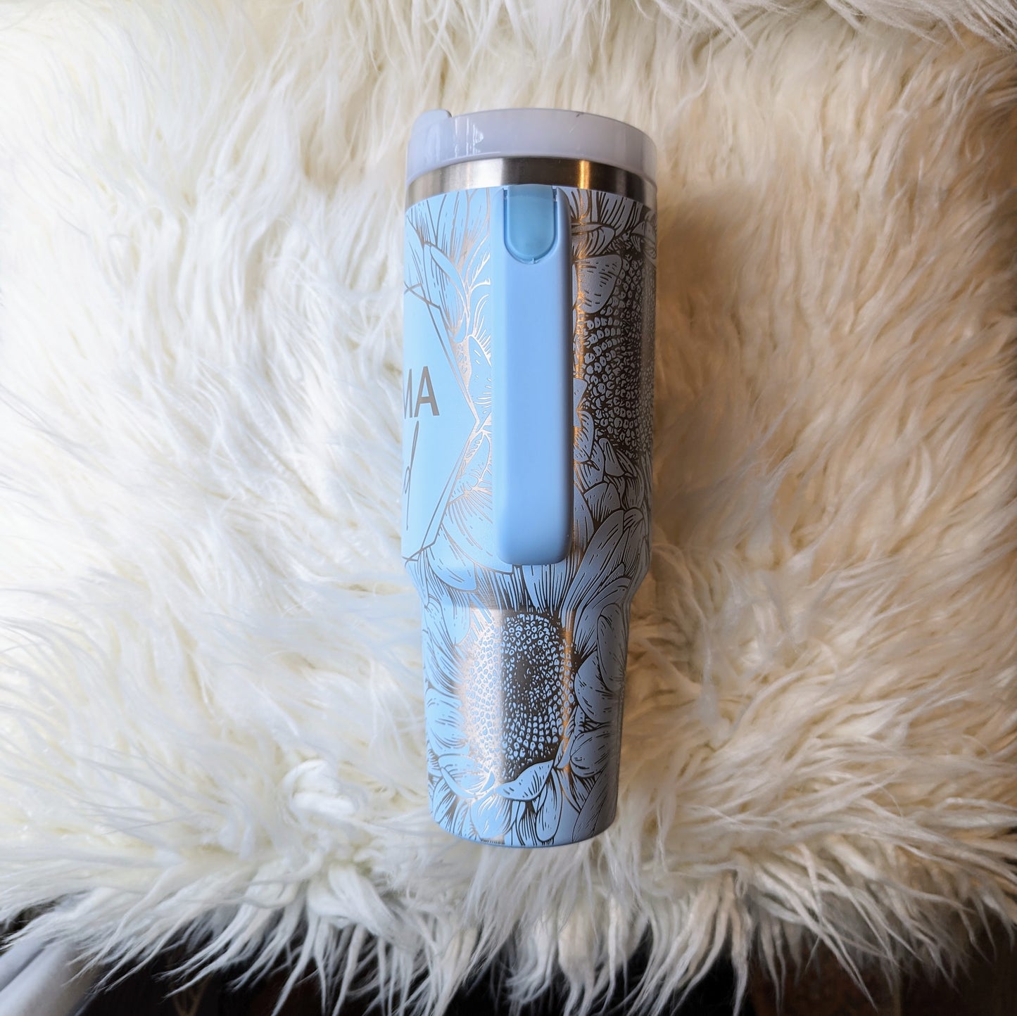 Photo of a soft blue colored 40 oz insulated tumbler with handle permanently engraved with a sunflower pattern and the text Mama Tried