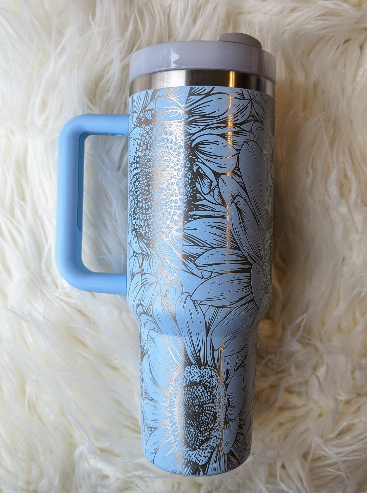 Photo of a soft blue colored 40 oz insulated tumbler with handle permanently engraved with a sunflower pattern and the text Mama Tried