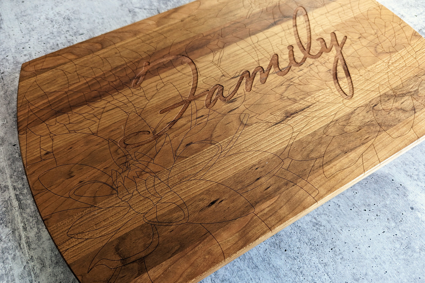 Close up view of a solid cherry wood cutting board with floral markings and the word Family engraved in the center to show the floral marking in detail.