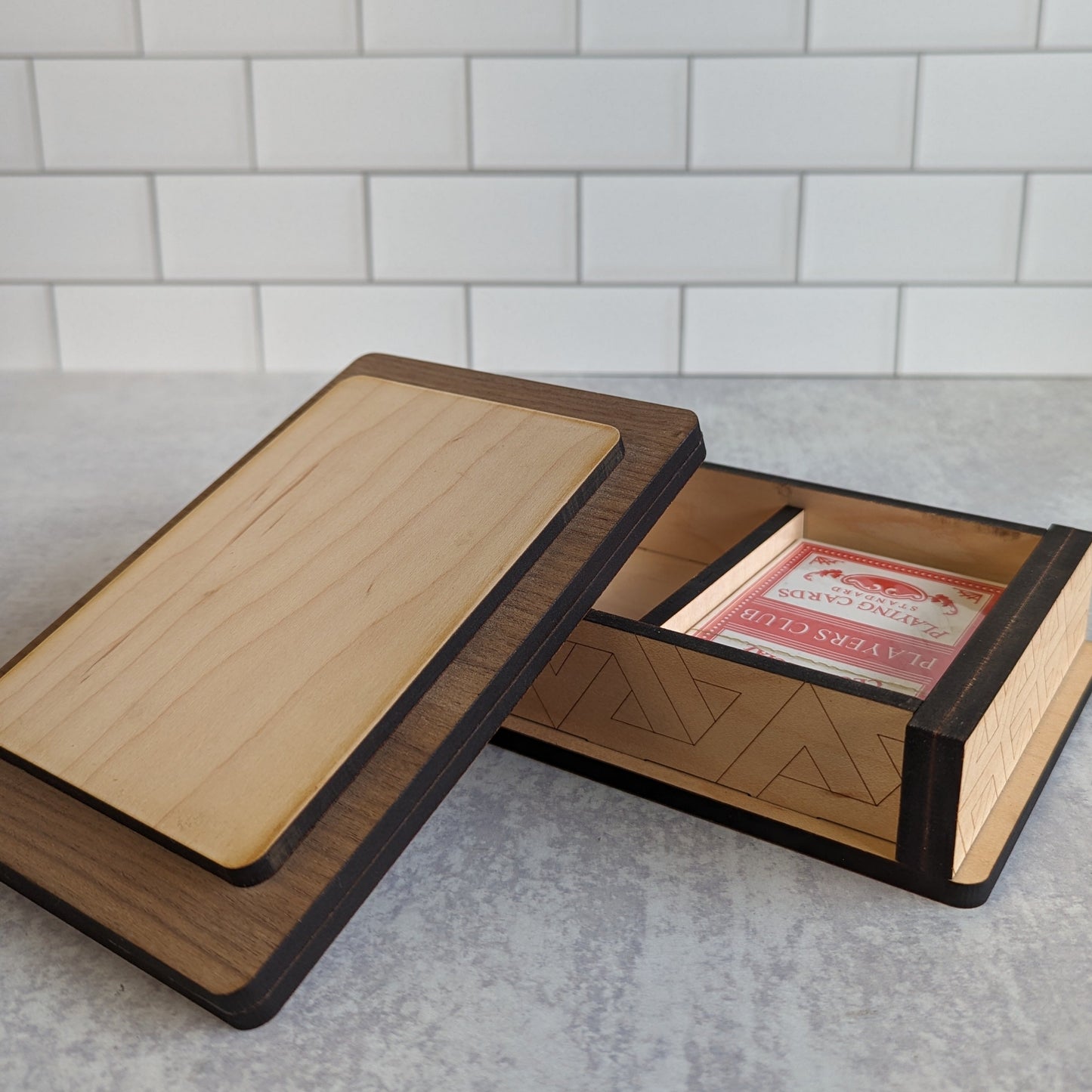 Handcrafted wooden playing card box made with layered walnut, maple, and mahogany veneer. Intricate geometric design on the lid with rich natural tones. Designed to hold two standard decks of cards.