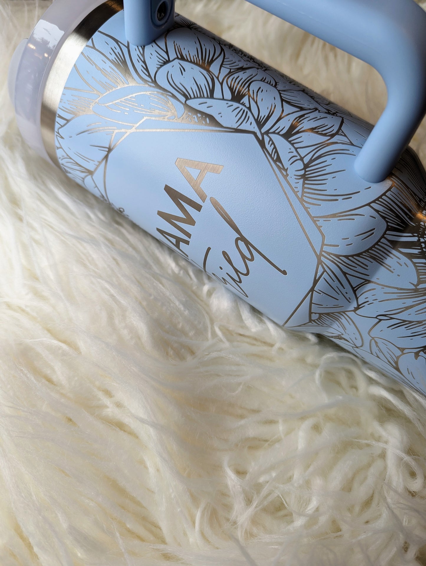 Photo of a soft blue colored 40 oz insulated tumbler with handle permanently engraved with a sunflower pattern and the text Mama Tried