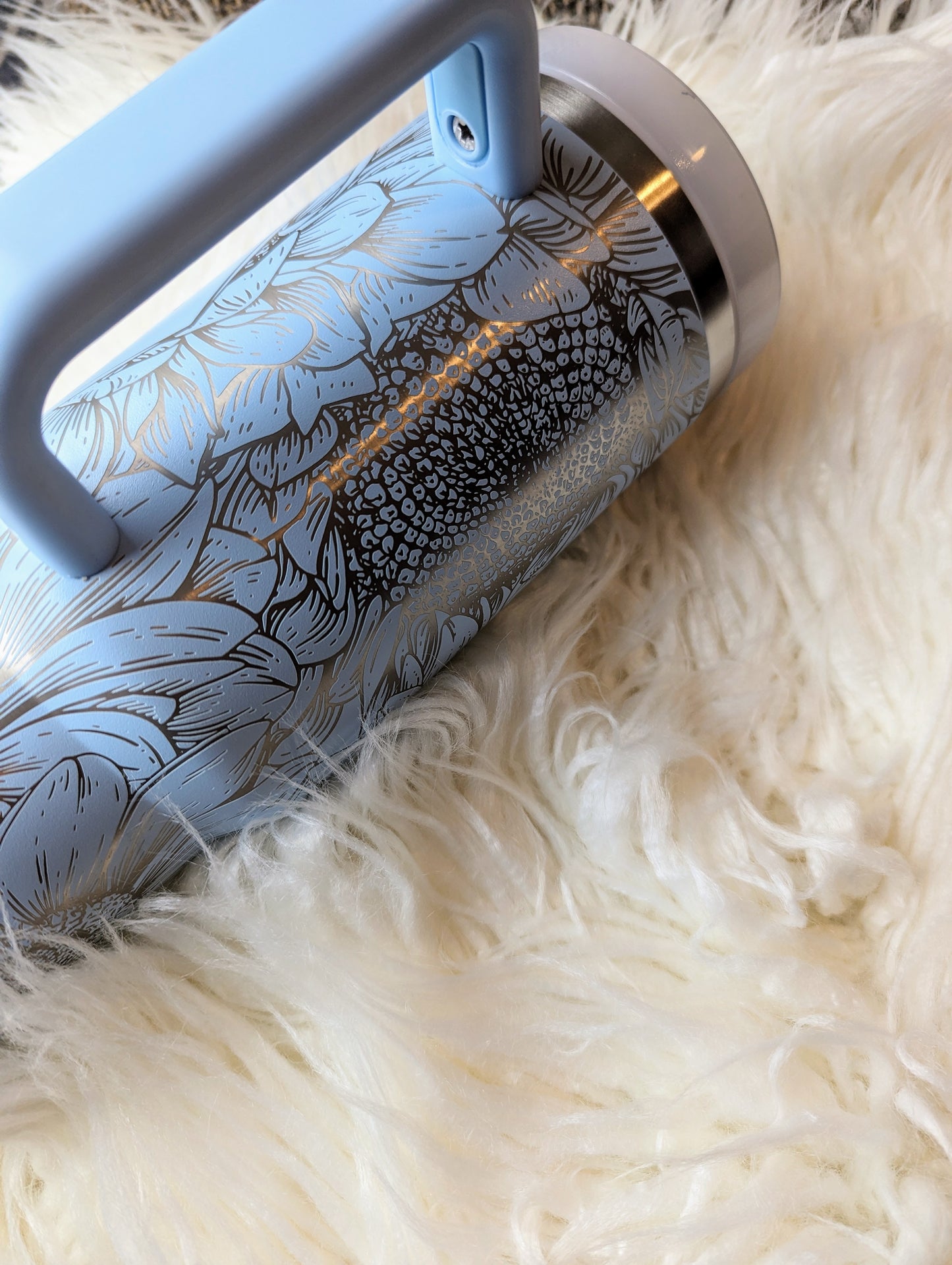 Photo of a soft blue colored 40 oz insulated tumbler with handle permanently engraved with a sunflower pattern and the text Mama Tried