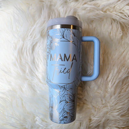 Photo of a soft blue colored 40 oz insulated tumbler with handle permanently engraved with a sunflower pattern and the text Mama Tried