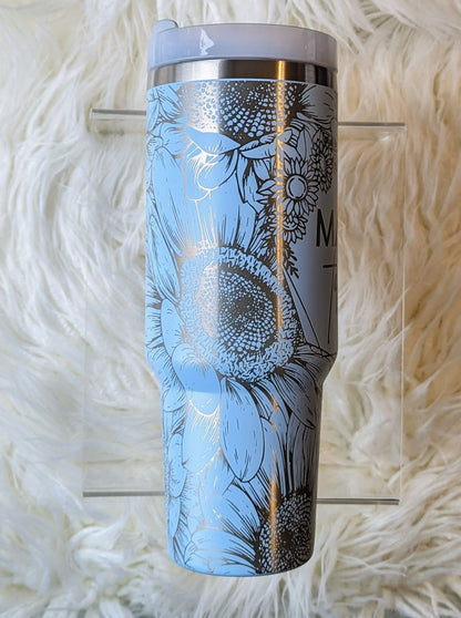 Photo of a soft blue colored 40 oz insulated tumbler with handle permanently engraved with a sunflower pattern and the text Mama Tried