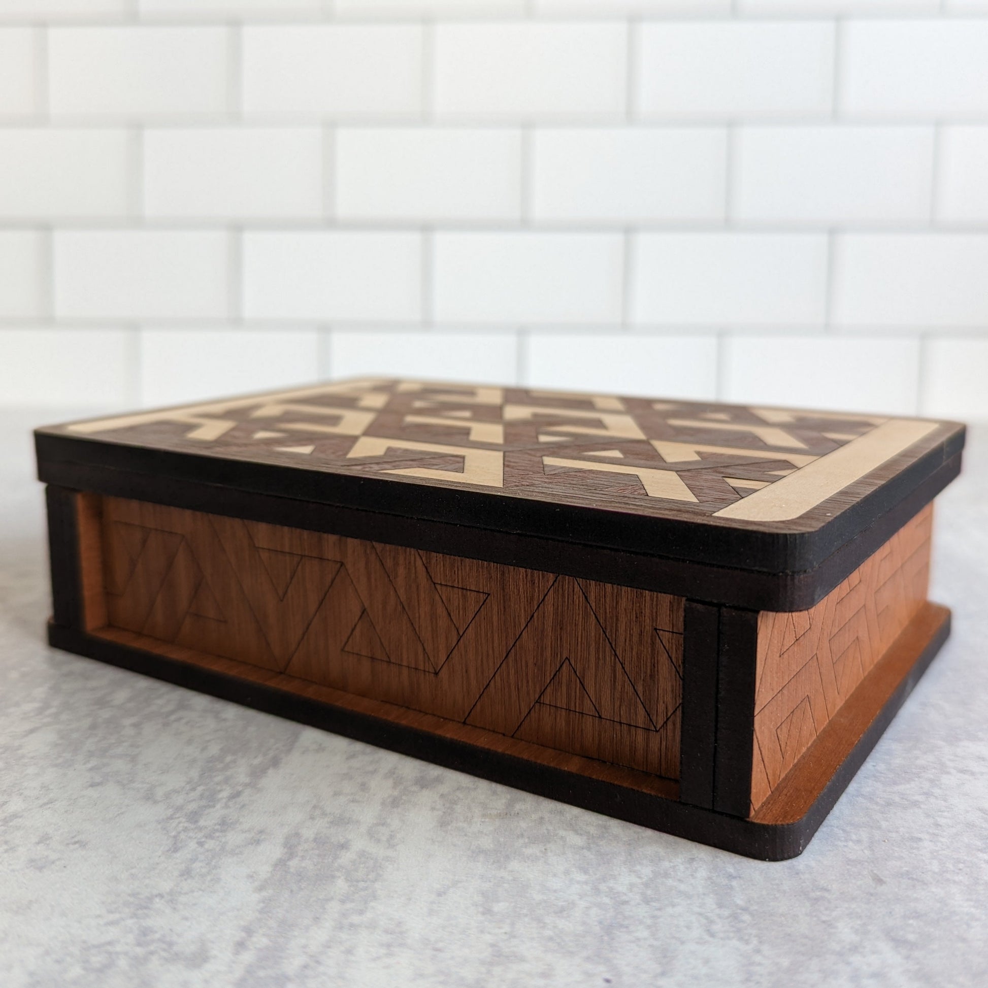 Handcrafted wooden playing card box made with layered cherry, walnut, maple, and mahogany veneer. Intricate geometric design on the lid with rich natural tones. Designed to hold two standard decks of cards.
