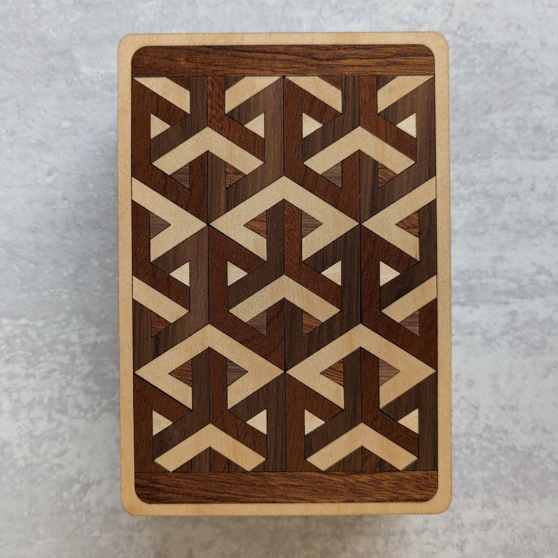 Handcrafted wooden playing card box made with layered cherry, walnut, maple, and mahogany veneer. Intricate geometric design on the lid with rich natural tones. Designed to hold two standard decks of cards.
