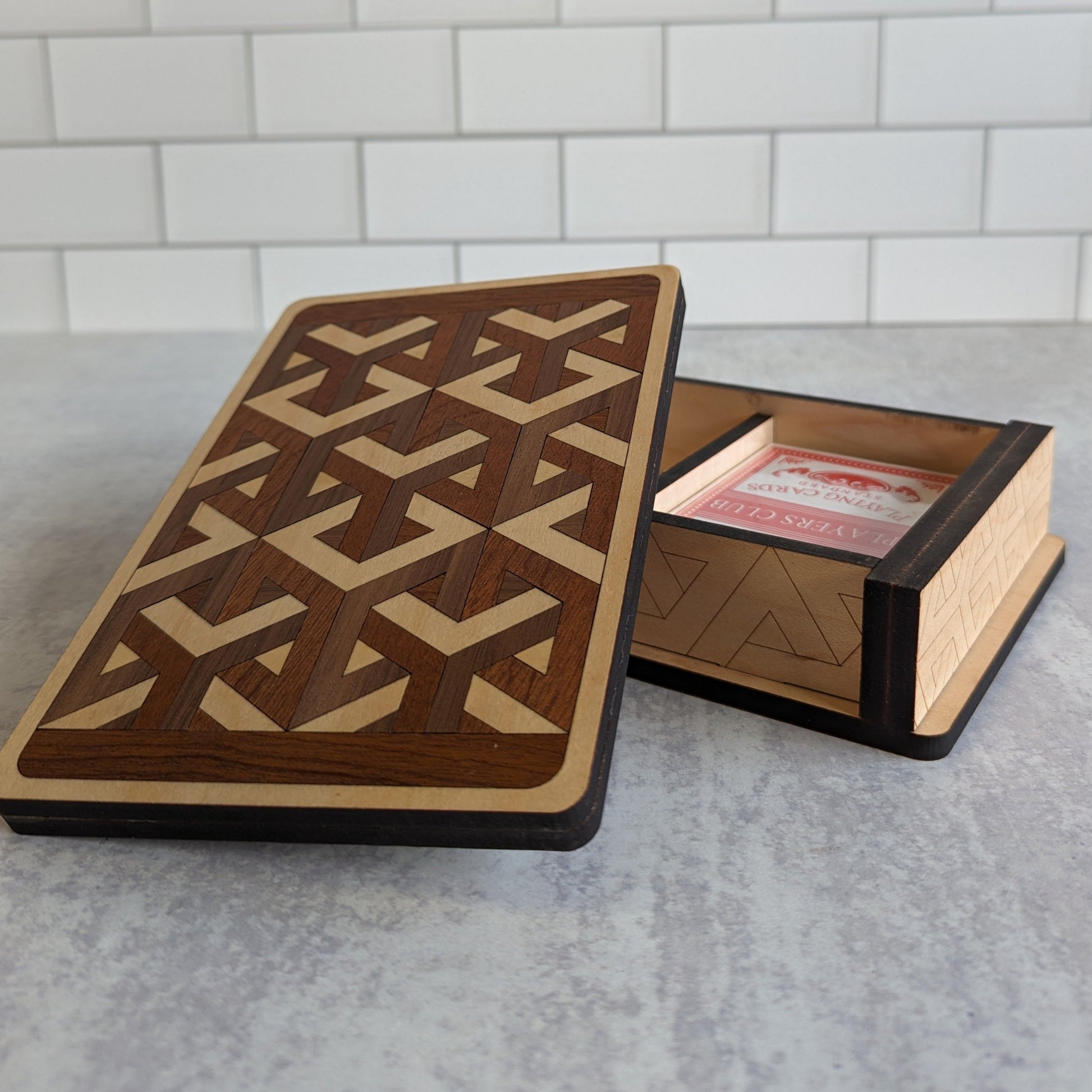 Handcrafted wooden playing card box made with layered cherry, walnut, maple, and mahogany veneer. Intricate geometric design on the lid with rich natural tones. Designed to hold two standard decks of cards.