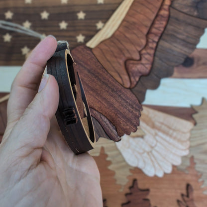 Hand holding a small wooden object with a detailed background of an eagle.